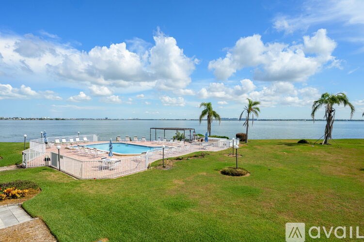 A pool surrounded by a grassy area with palm trees and a cloudy sky.
