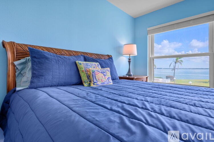 A bed with blue sheets and a window overlooking the ocean.