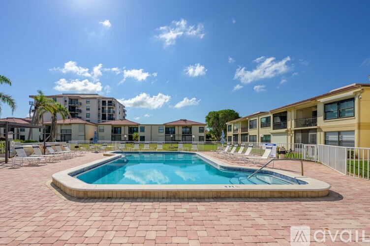 A pool surrounded by a brick patio and apartment buildings in the background.