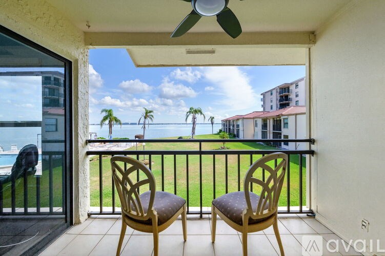Two chairs are on a balcony with a view of the ocean and palm trees.