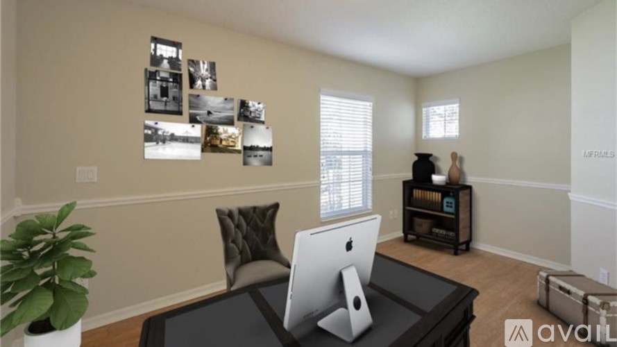 A room with a black table, a white monitor, and a brown pillow.
