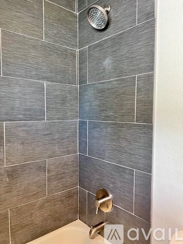 A shower with a grey tile wall and a silver faucet.