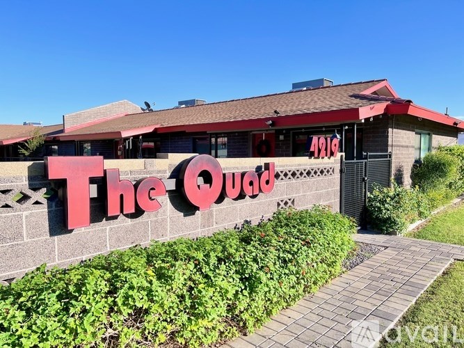 The Quad building with a red signboard and green bushes in front.