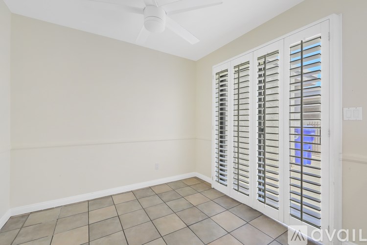 A room with a fan, tiled floor and a window with shutters.