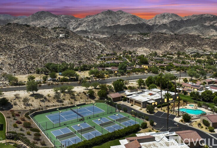 A tennis court is surrounded by houses and mountains.