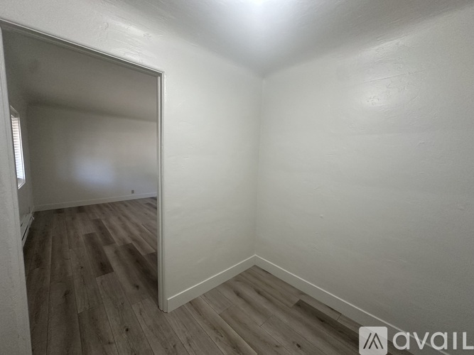 A room with wooden flooring and white walls, with a doorway leading to another room.