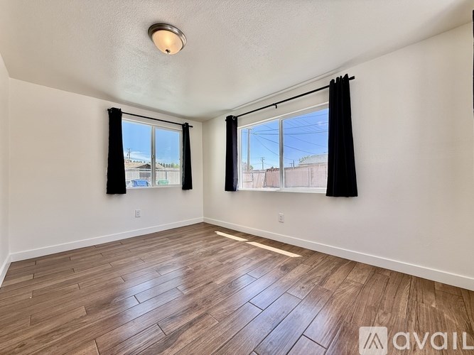 A room with wooden flooring and a window with black curtains.
