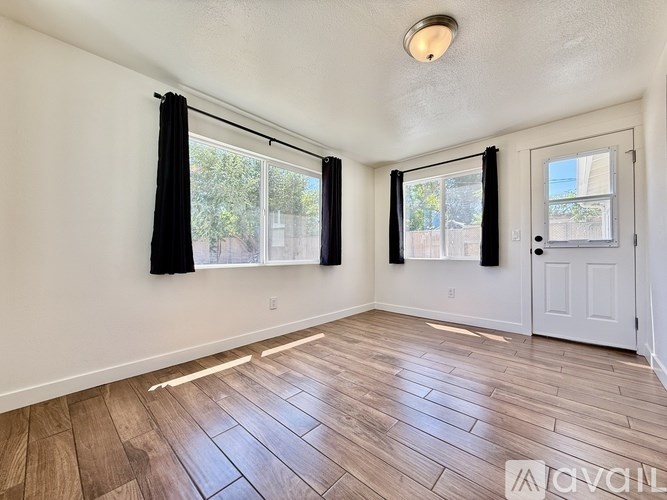 A room with wooden flooring and a window with black curtains.