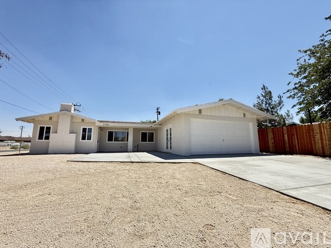 A white house with a garage is situated in a gravel lot.