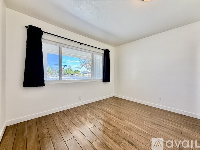 A room with wooden flooring and a window with black curtains.