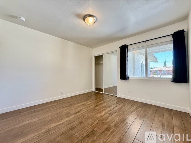 A room with wooden flooring and a window with black curtains.