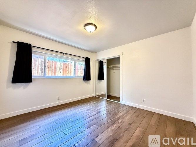 A room with wooden flooring and a window with black curtains.
