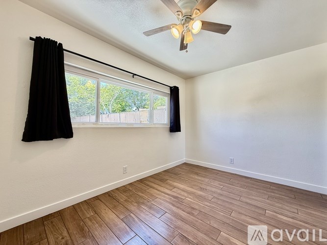 A room with a ceiling fan and a window with black curtains.