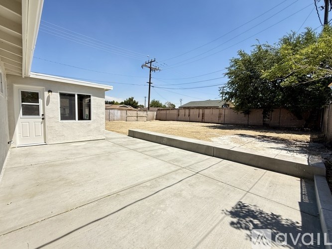 A sunny day in a backyard with a concrete patio and a white house.