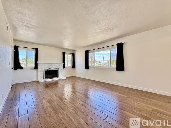 A room with wooden flooring and a fireplace with two windows.