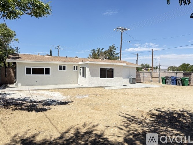 A white house with a brown roof is surrounded by a dirt lot.