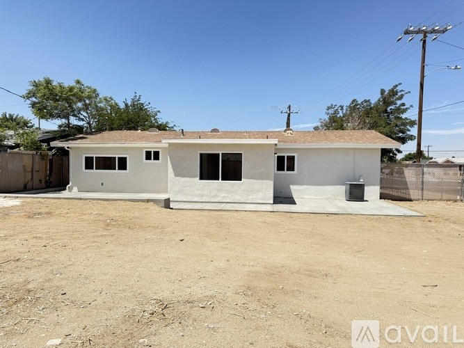 A two-story house with a brown roof and white walls is surrounded by a dirt lot.