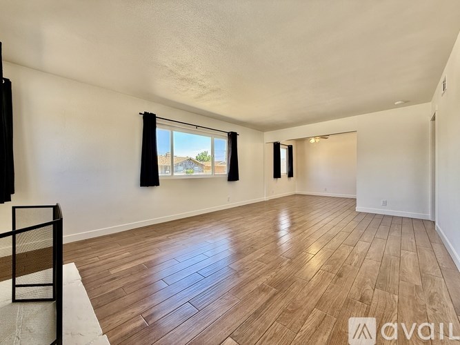 A room with wooden flooring and a window with black curtains.