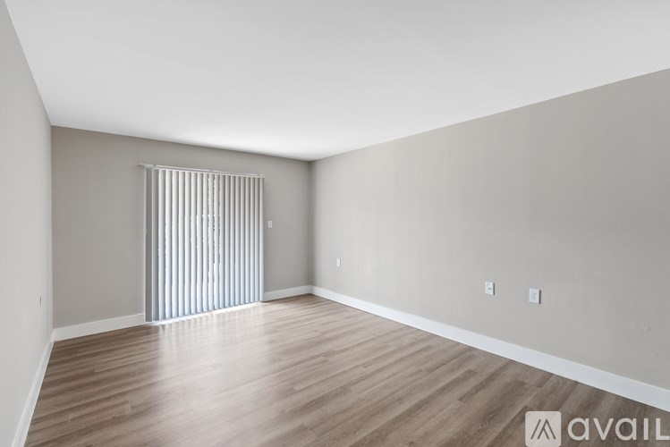 A room with wooden flooring and a window with vertical blinds.