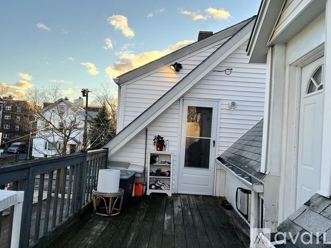 A small white house with a deck and a hot water heater.