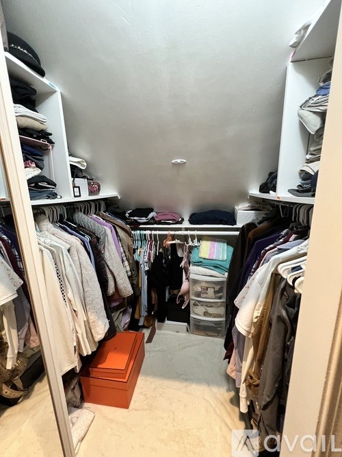 A small closet with clothes hanging on shelves and a box on the floor.