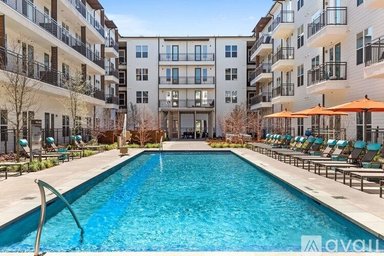 A large swimming pool in front of apartment buildings with lounge chairs and umbrellas.