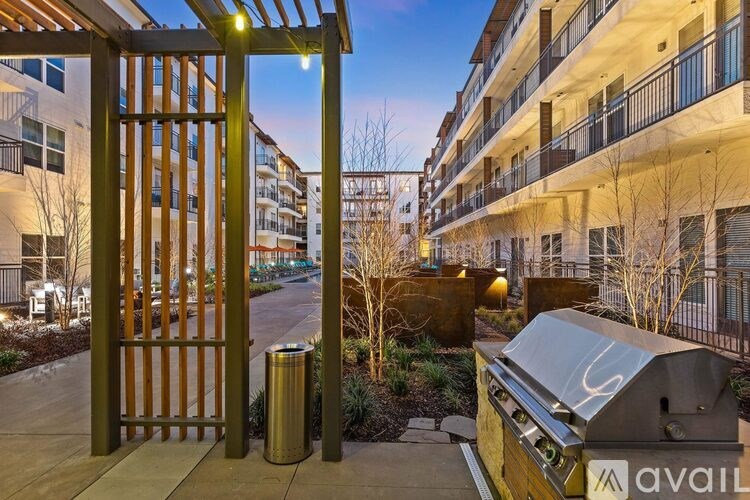 A modern gate leads to a courtyard with a trash can and a BBQ grill.