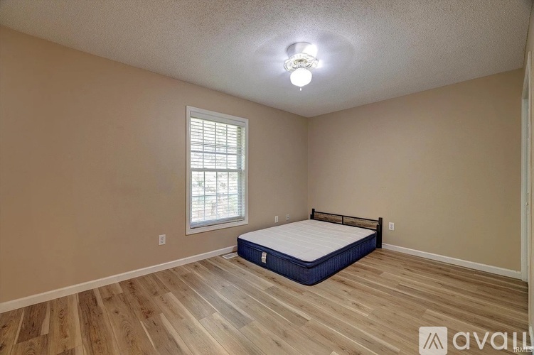 A bedroom with a bed, wooden floors, and a window with blinds.