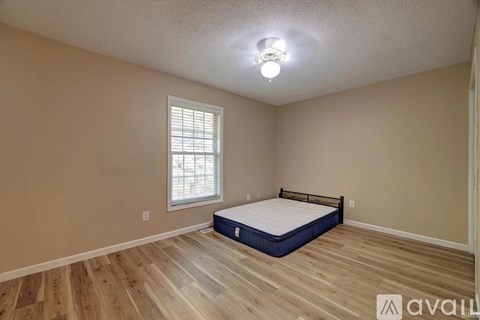 A bedroom with a bed, wooden floors, and a window with blinds.