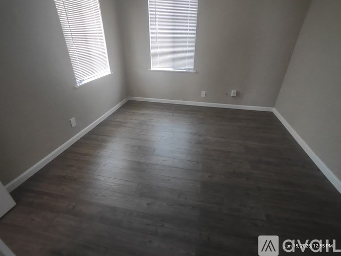 A room with wooden flooring and two windows.
