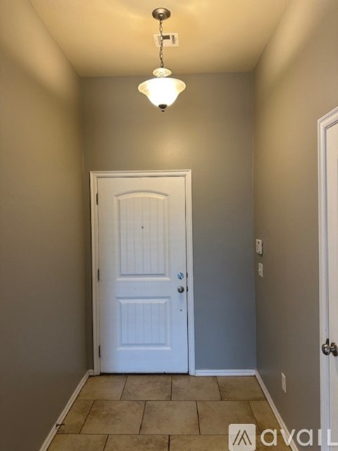 A grey door is at the end of a hallway with a brick wall on one side and a plant on the other.