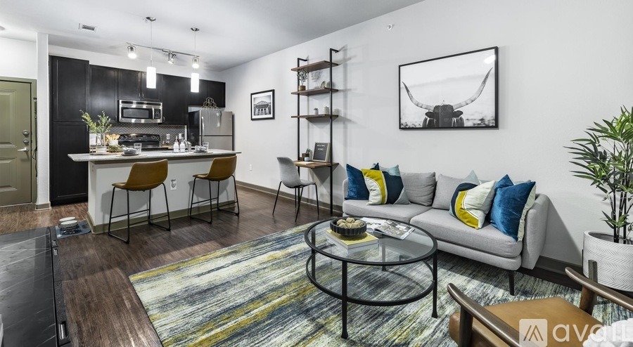 A modern living room with a grey sofa, a glass coffee table, and a kitchen area in the background.