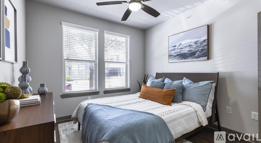 A bedroom with a bed, a ceiling fan, and a painting on the wall.