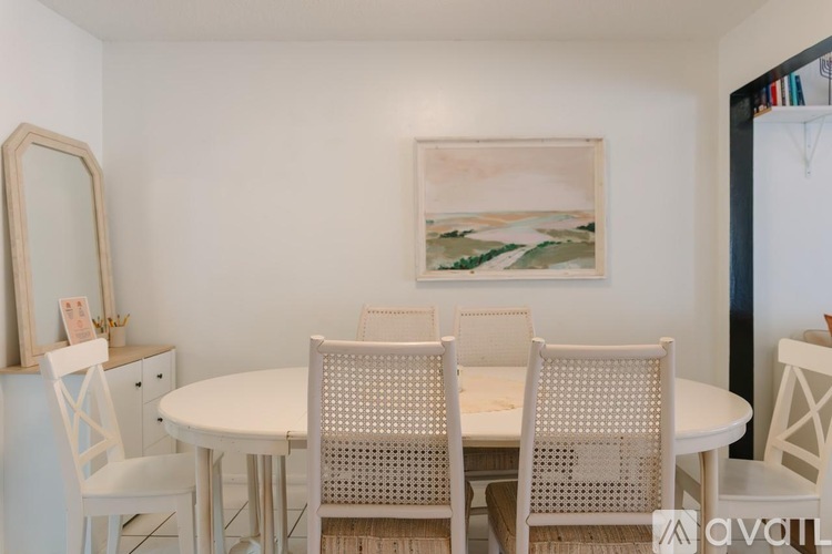 A white dining table with four chairs and a painting on the wall.