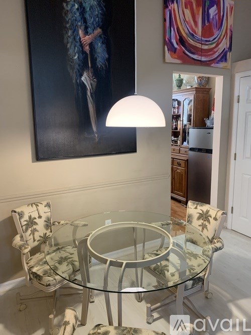 A glass table with a painting of a woman in blue feathers on the wall.