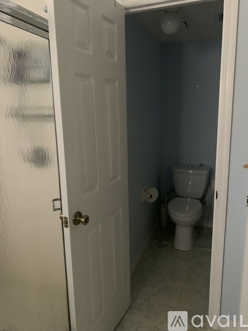 A white door with a gold handle is open to a bathroom with a toilet and a white sink.