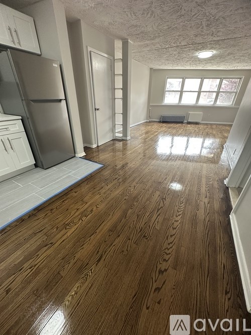 A kitchen with a refrigerator, cabinets, and a wooden floor.