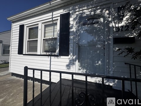 A white house with a black railing and a window with a closed shutter.