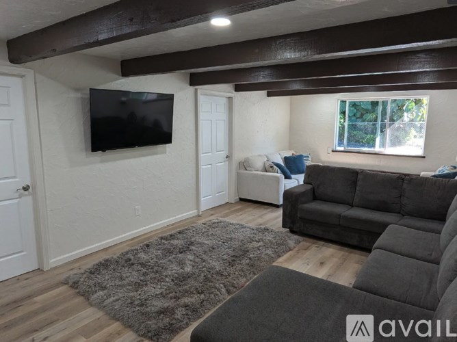 A living room with a grey rug, a black couch, and a flat screen TV mounted on the wall.