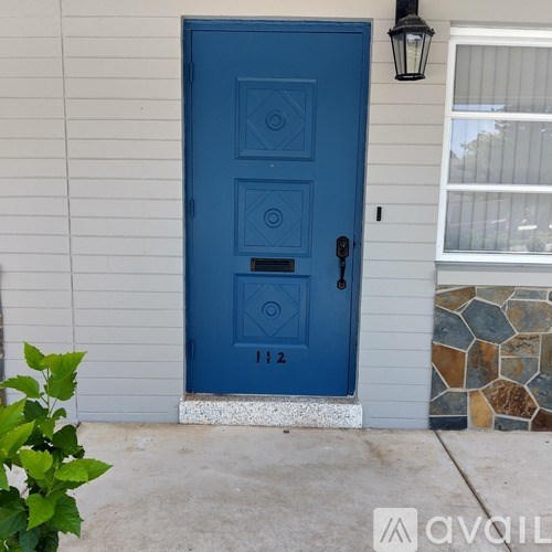 A blue door with a black handle and a mail slot is on a white siding house.