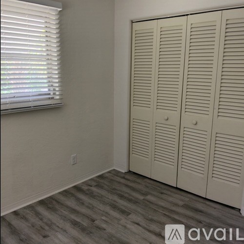 A room with a window, wooden floor and a white wardrobe.