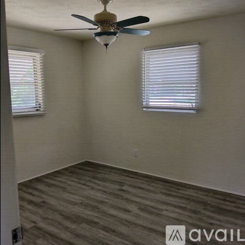 A room with a ceiling fan and two windows with blinds.