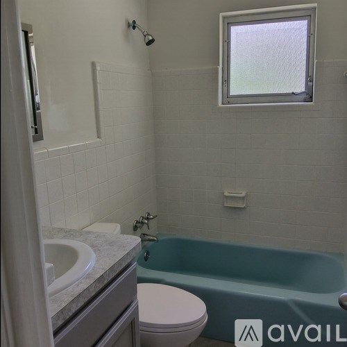 A bathroom with a blue bathtub, white toilet, and a window.