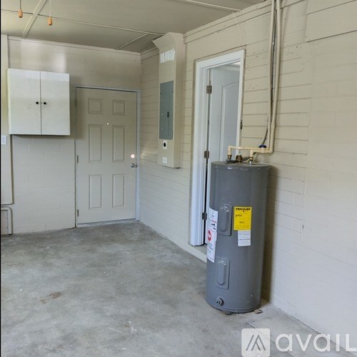 A grey water heater sits in a room with white walls and a door.