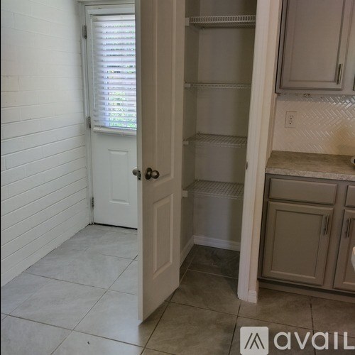 A white door is open to a kitchen with white cabinets.