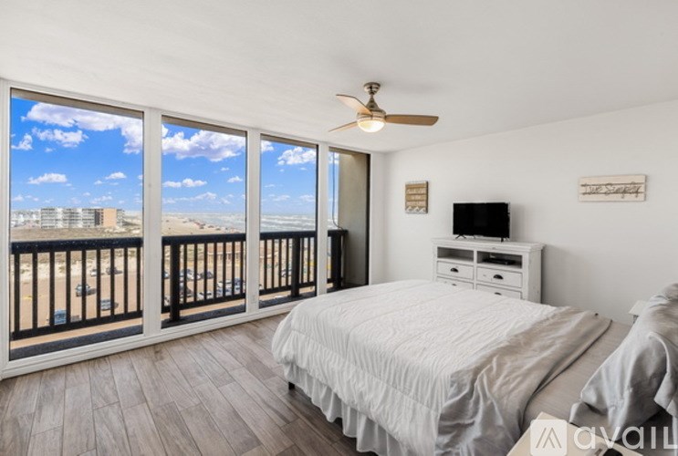 A bedroom with a large bed, a ceiling fan, and a balcony with a view of the beach.