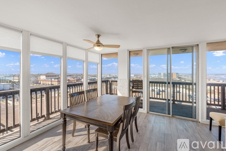A dining room with a table and chairs overlooking a balcony with a view of the beach.