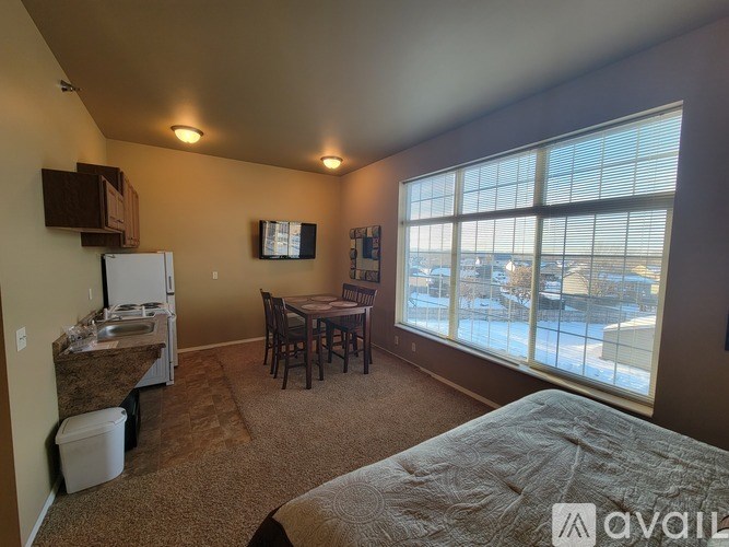 A bedroom with a bed, a table and chairs, and a refrigerator.