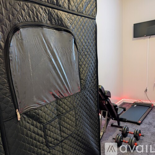 A black, diamond-patterned sleeping bag in a room with a TV and gym equipment.