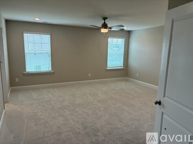 A room with a carpeted floor, a ceiling fan, and two windows.